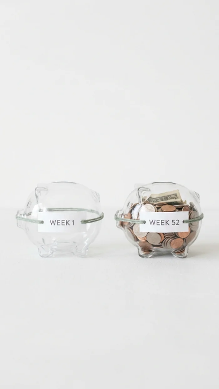 Two small glass piggy banks side by side labeled Week 1 and Week 52, one nearly empty and one full of cash and coins